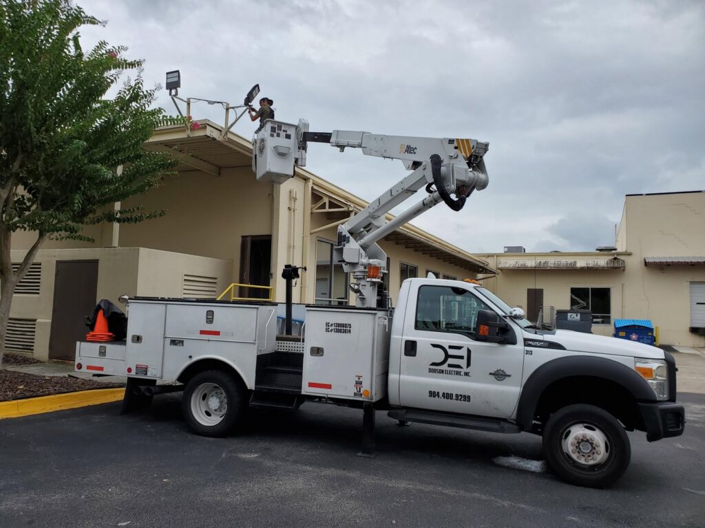 An electrician in a bucket truck repairing a light fixture on a building roof for Dobson Electric, Inc. in Jacksonville, FL.