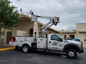 An electrician in a bucket truck repairing a light fixture on a building roof for Dobson Electric, Inc. in Jacksonville, FL.