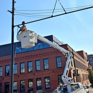An electrician in a bucket truck working on utility lines and a pole for Power City Electric in Spokane, WA.