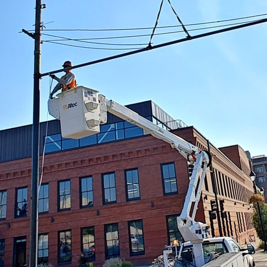 An electrician in a bucket truck working on utility lines and a pole for Power City Electric in Spokane, WA.