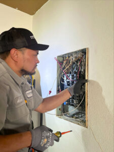 An Electricode electrician inspecting an open electrical panel with a voltage tester in Las Vegas, NV.