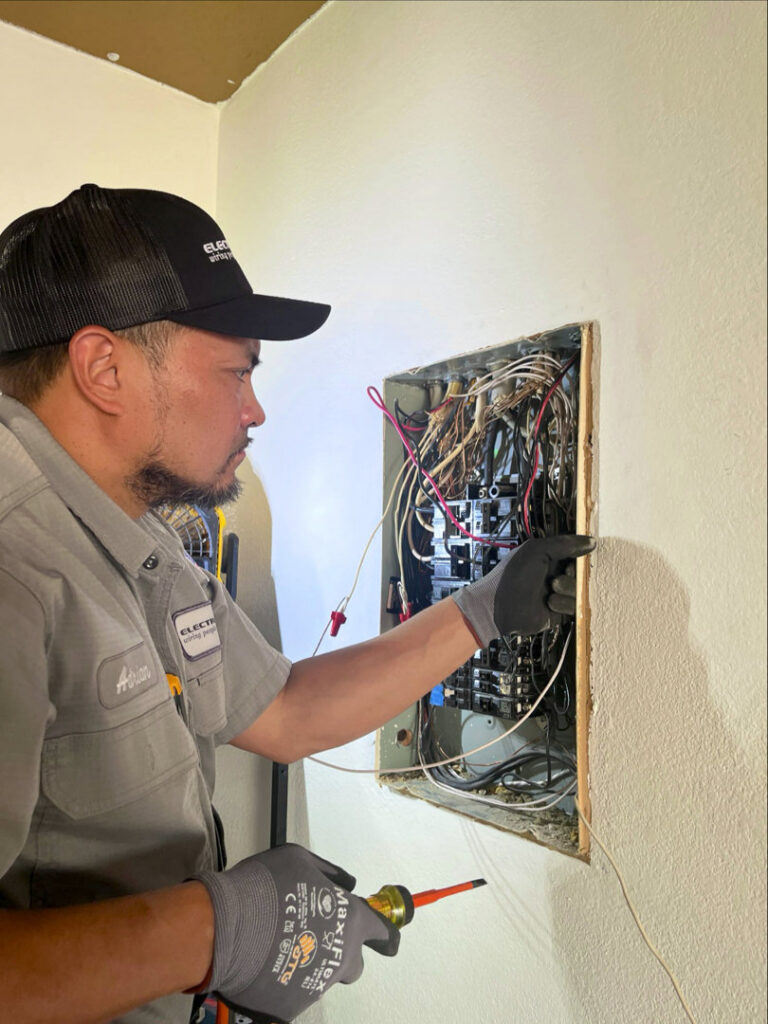 An Electricode electrician inspecting an open electrical panel with a voltage tester in Las Vegas, NV.