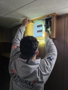 An electrician from National Electric - Lansing inspecting an electrical panel with a headlamp in Lansing, MI.