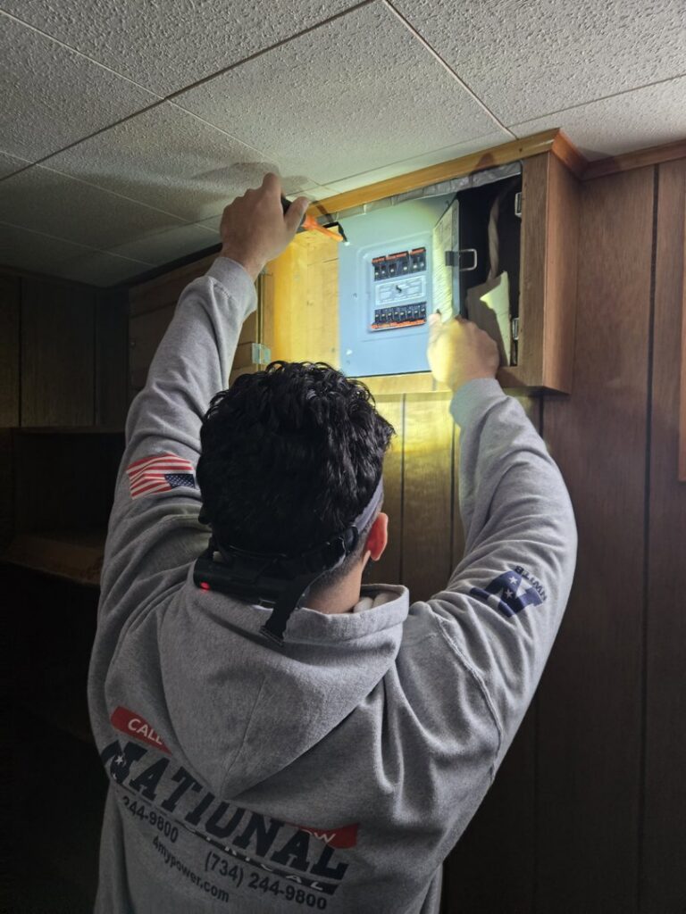 An electrician from National Electric - Lansing inspecting an electrical panel with a headlamp in Lansing, MI.