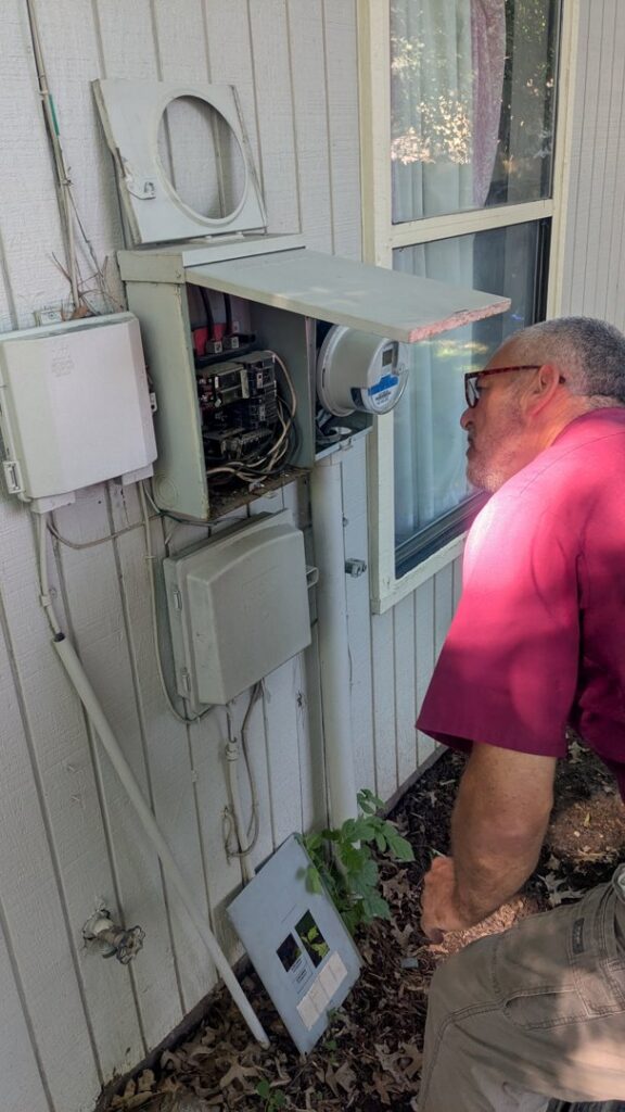 An electrician from Murray Electric & Plumbing inspecting an outdoor electrical panel and meter box in Broken Arrow, OK.