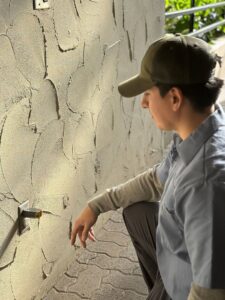 An electrician inspecting an outdoor electrical outlet on a textured wall for Three Rivers Electric in Fort Wayne, IN.