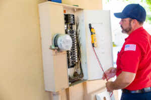 An electrician from Minuteman Home Services inspecting an outdoor electrical panel with a tester in Mesa, AZ