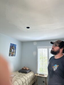An electrician inspecting a recessed light fixture opening in a ceiling for Steve Cavenee Electric in Orange, CA.