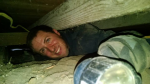 An electrician inspecting wiring in a crawl space with a flashlight for Kavanagh Electric in Fresno, CA.