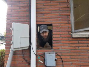 An electrician from Vets Electric Company inspecting wiring through an opening in a brick wall in Tacoma, WA
