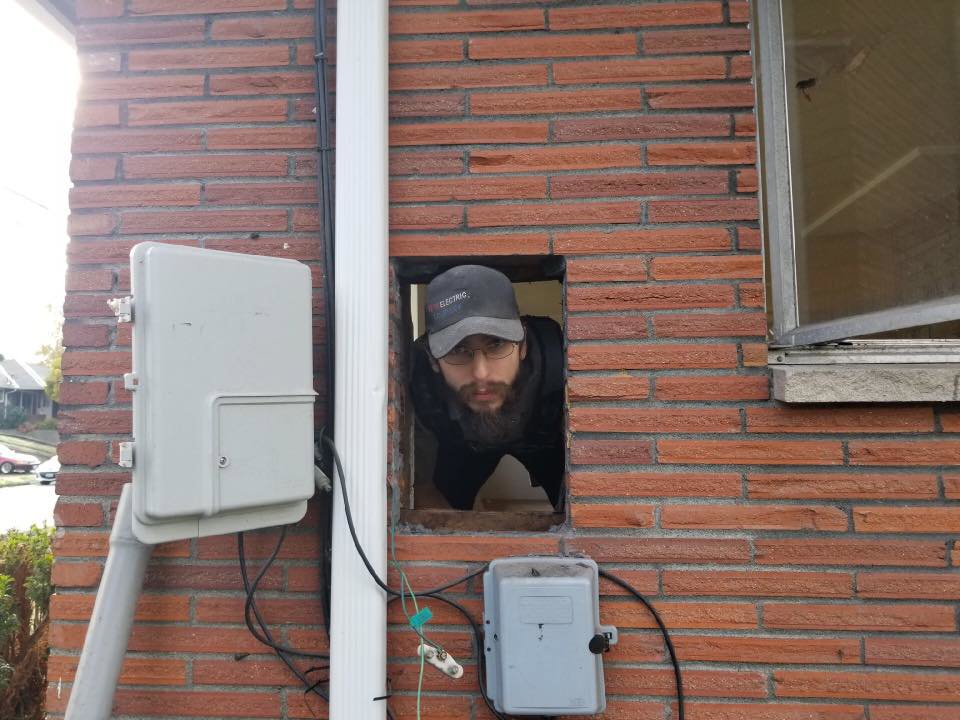 An electrician from Vets Electric Company inspecting wiring through an opening in a brick wall in Tacoma, WA