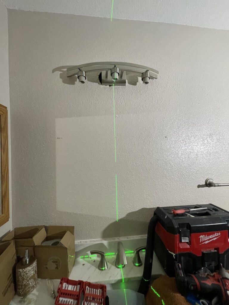 An electrician using a laser level to install a bathroom light fixture for Rogers Family Handyman in Chandler, AZ