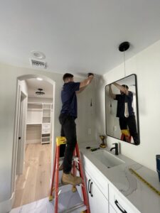 An electrician on a ladder installing a new light fixture in a bathroom for Miller and Sons Electric in North Myrtle Beach, SC.