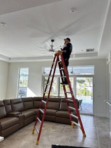 An electrician from Bee Electrical Contracting on a ladder installing a ceiling fan in Port Saint Lucie, FL.