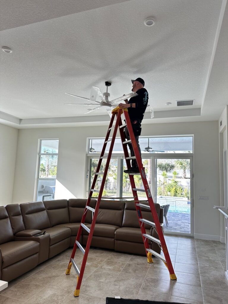 An electrician from Bee Electrical Contracting on a ladder installing a ceiling fan in Port Saint Lucie, FL.