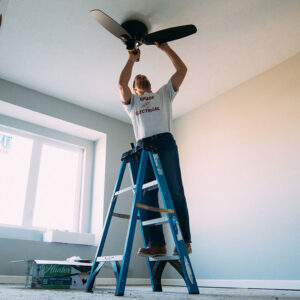 An electrician installing a new ceiling fan on a ladder for Brase Electrical Contracting Corp in Omaha, NE.