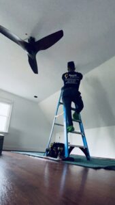 An electrician from Royal Electric Services on a ladder installing a ceiling fan in Raleigh, NC