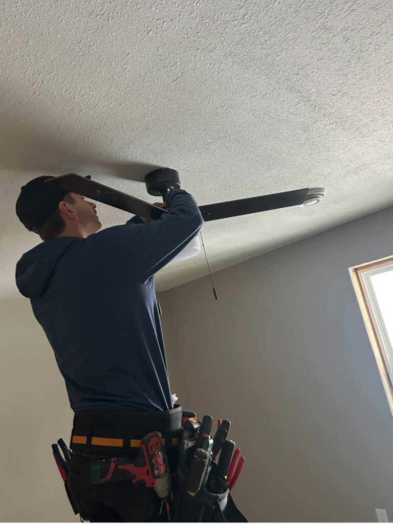 An electrician on a ladder installing a new ceiling fan for a client of LeBrun Electric, Heating & Cooling in Brooklyn Park, MN.