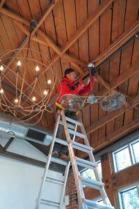 An electrician on a ladder installing a ceiling fan and light fixture for Electrical Power Source in Fresno, CA.