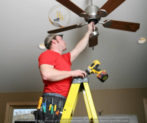 An electrician installing a ceiling fan on a ladder, providing expert service for Power Pro Electricians Roanoke, VA