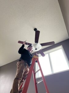 An electrician on a ladder installing or repairing a ceiling fan for LeBrun Electric, Heating & Cooling in Brooklyn Park, MN.