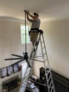 An electrician from Revamp Athens Electrical Company installing a new ceiling fan in Athens, GA.