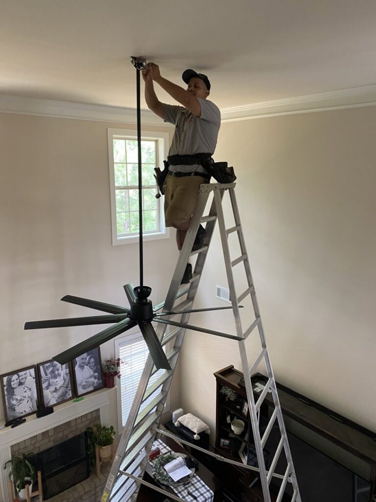An electrician from Revamp Athens Electrical Company installing a new ceiling fan in Athens, GA.