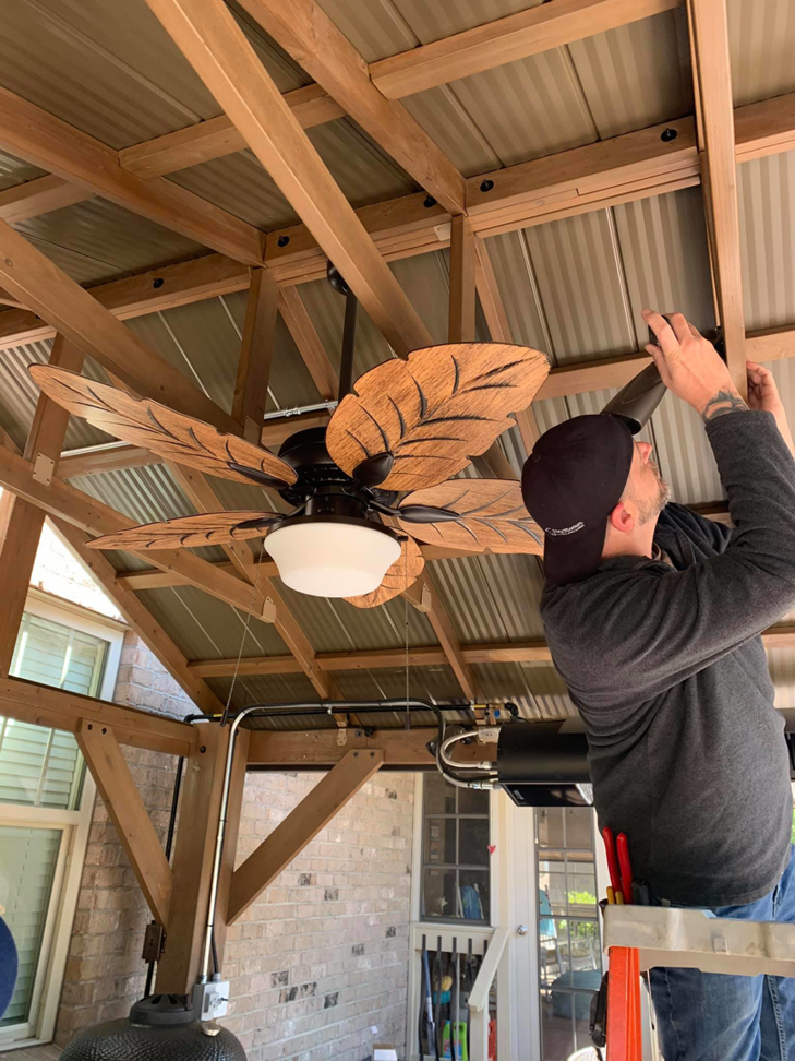 An electrician from Volt Doctors Raleigh, NC, installing a decorative ceiling fan in an outdoor living space.