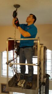 An electrician on a lift installing a large ceiling light fixture for Peace Of Mind Services in Sag Harbor, NY