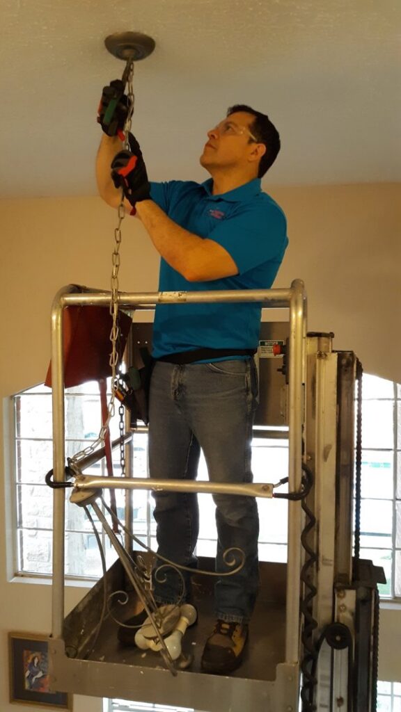 An electrician on a lift installing a large ceiling light fixture for Peace Of Mind Services in Sag Harbor, NY