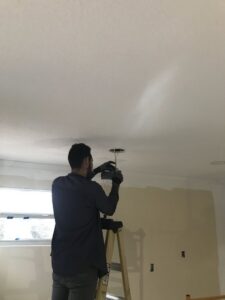An electrician from 60HZ Electric on a ladder, installing a ceiling light fixture in St. Petersburg, FL.