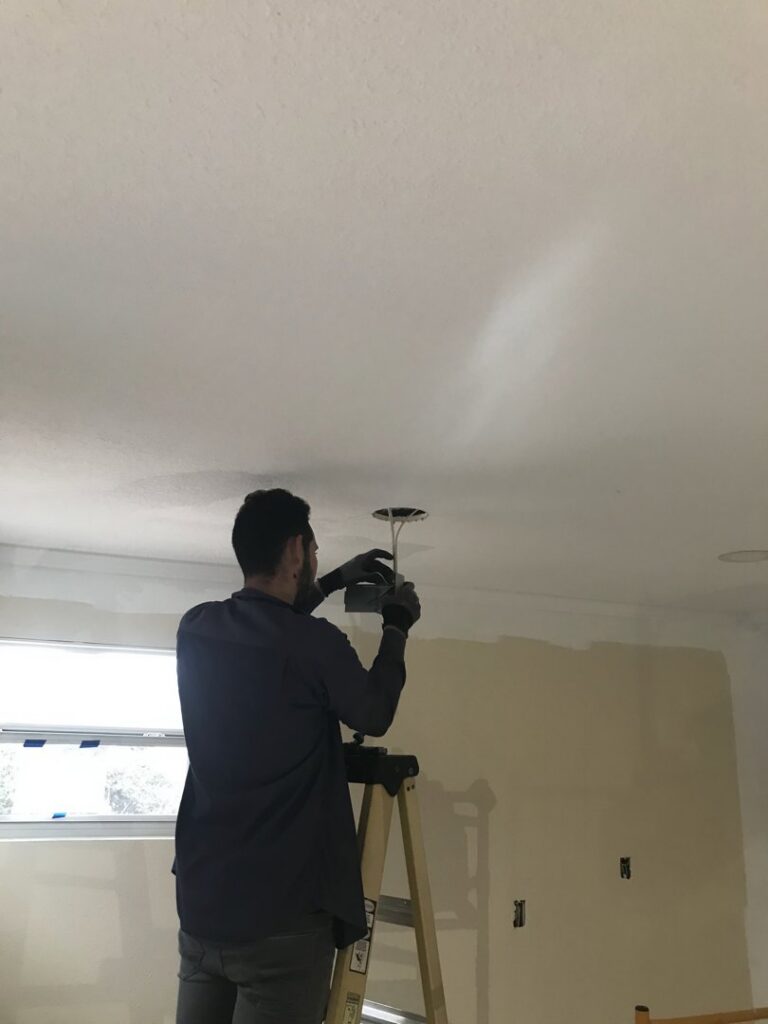 An electrician from 60HZ Electric on a ladder, installing a ceiling light fixture in St. Petersburg, FL.