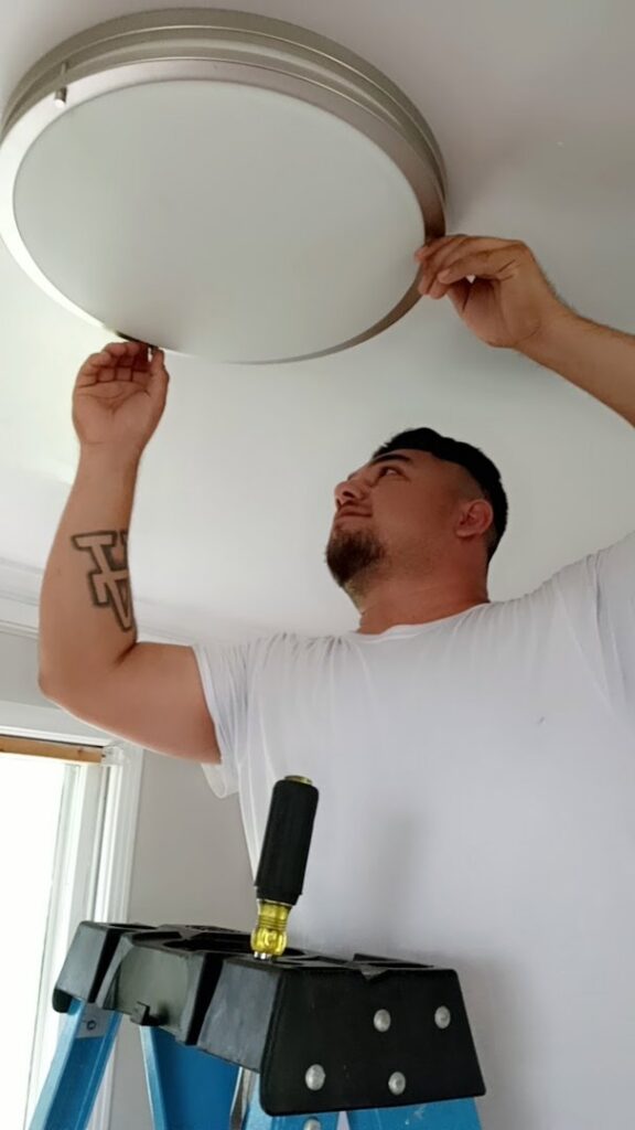 An electrician on a ladder installing a new ceiling light fixture for a client of Delta Electric in Germantown, MD.