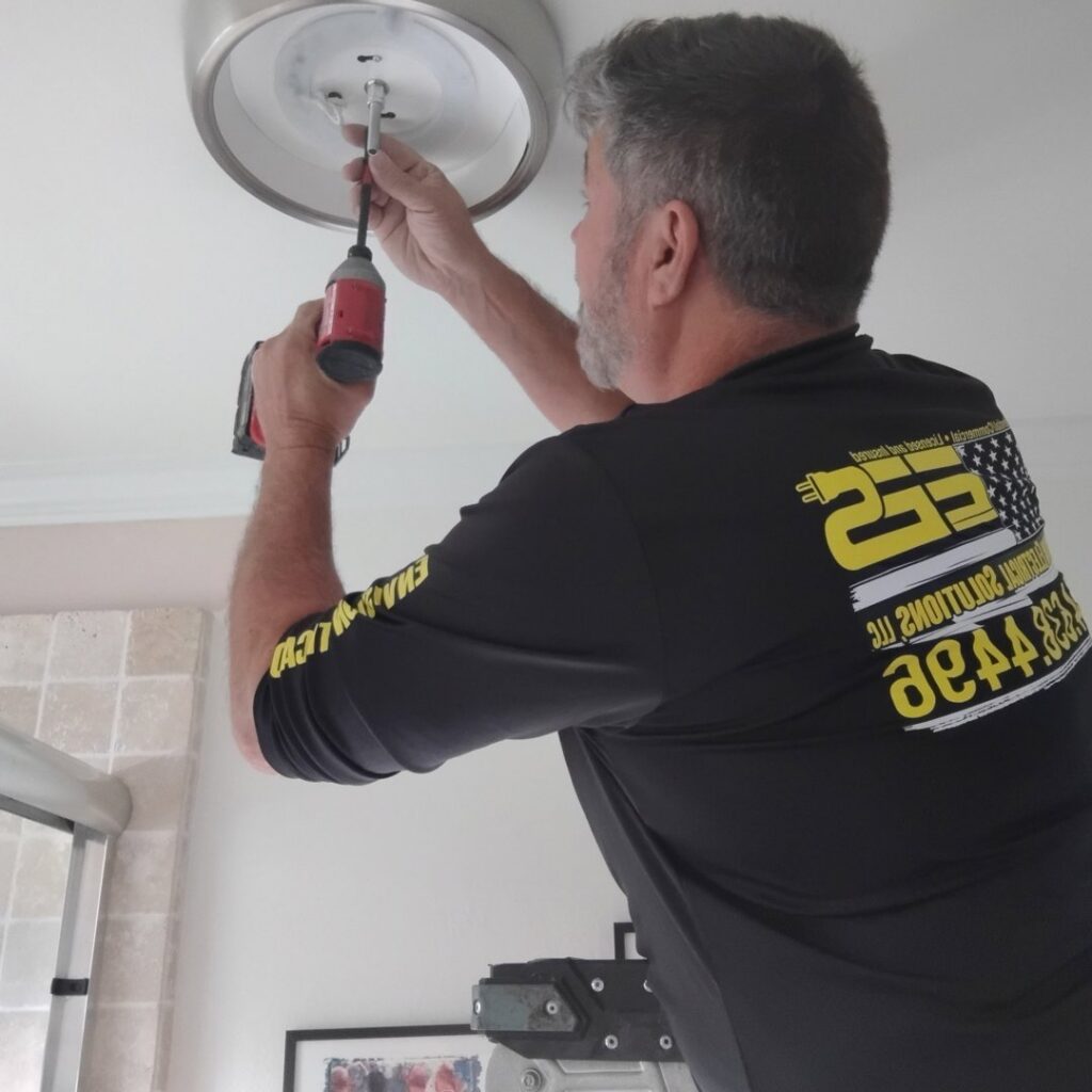 An electrician from Envision Electrical Solutions installing a ceiling light fixture with a power drill in Fort Lauderdale, FL.