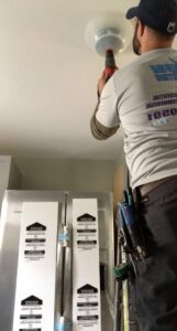 An electrician from Surge Electric LLC on a ladder, installing a ceiling light fixture with a drill in Youngstown, OH.