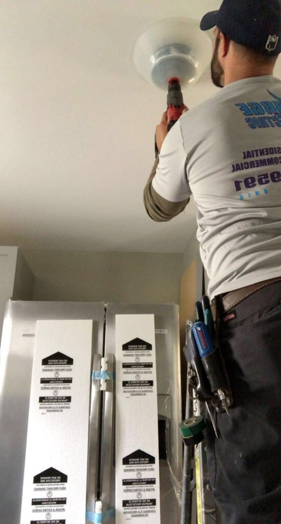 An electrician from Surge Electric LLC on a ladder, installing a ceiling light fixture with a drill in Youngstown, OH.