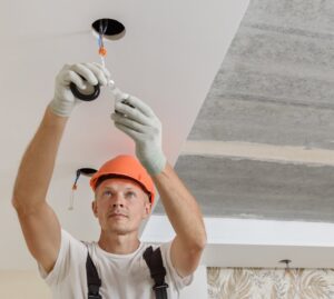 An electrician in a hard hat and gloves installing wiring for recessed ceiling lights, a service by Beaver Electric in Hillsboro, OR.