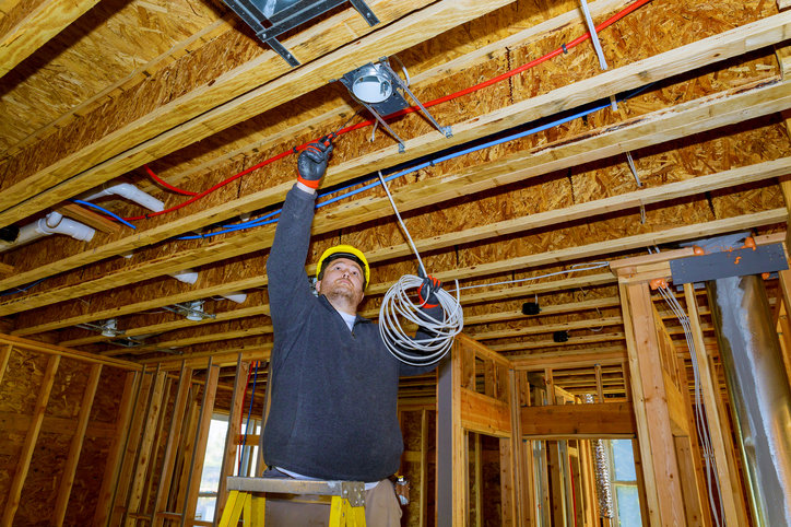 An electrician on a ladder installing electrical wiring in a ceiling during construction for BrotherlyLove Electric LLC in Houston, TX.