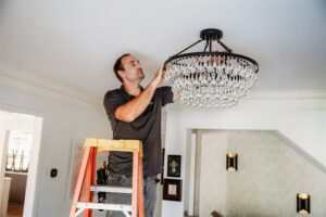 An electrician from Arnold Electrical Repair & Installation on a ladder installing a decorative chandelier in a home in Chicago, IL.