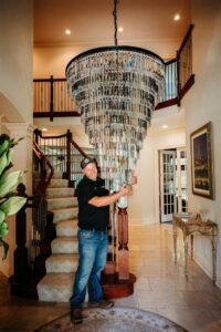 An electrician from Arnold Electrical Repair & Installation installing a large, multi-tiered chandelier in a home's entryway in Chicago, IL.