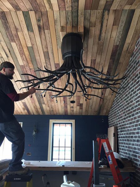 An electrician installing a large, decorative chandelier for President, Cannizzo Electric, Inc. in Rochester, NY.