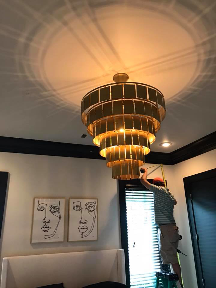 An electrician from Cothern Electric, LLC installing a large, tiered chandelier in Jonesboro, AR.