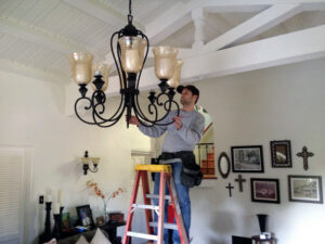 An electrician from Full Armor Services, LLC installing a large chandelier in a home in Meridian, ID.