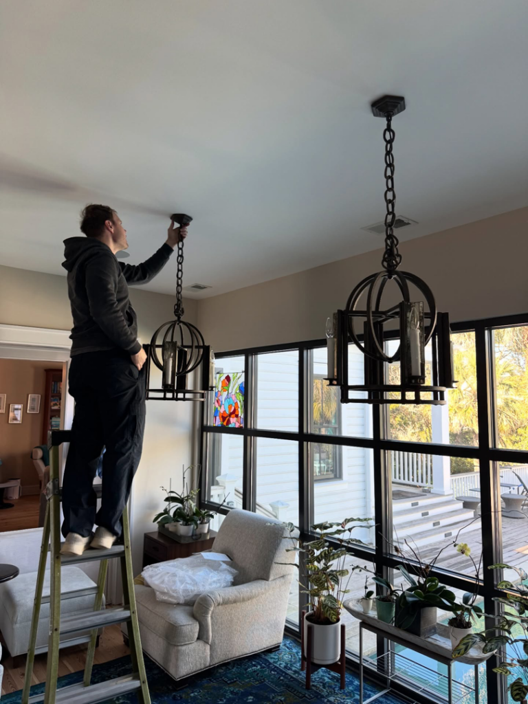An electrician installing a new chandelier in a home for Gloudeman Electric in Mount Pleasant, SC