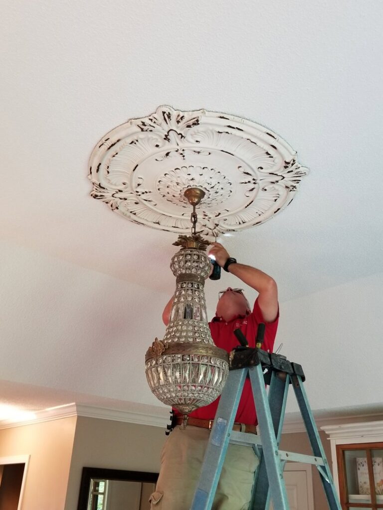 An electrician installing a large chandelier on a ceiling for John Kivel Electric, LLC in Woodbury, MN.