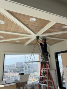 An electrician from Homestead Electric on a ladder installing a chandelier in a ceiling with recessed lights in Orem, UT.