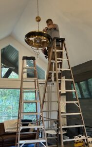 An electrician installing a large decorative chandelier in a high-ceiling room for Midway Electric in Columbia, MO