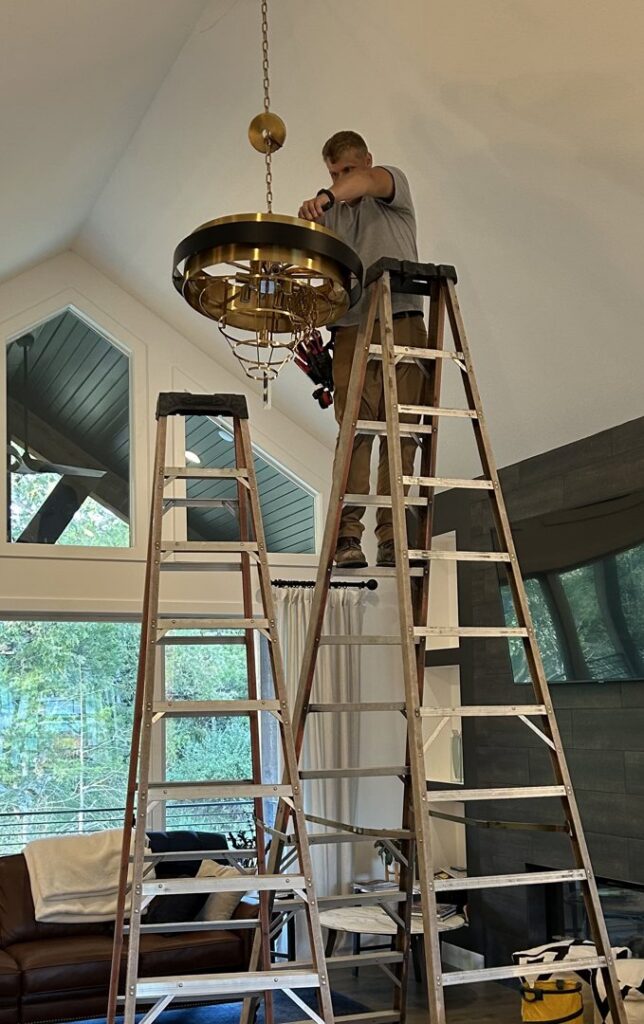 An electrician installing a large decorative chandelier in a high-ceiling room for Midway Electric in Columbia, MO