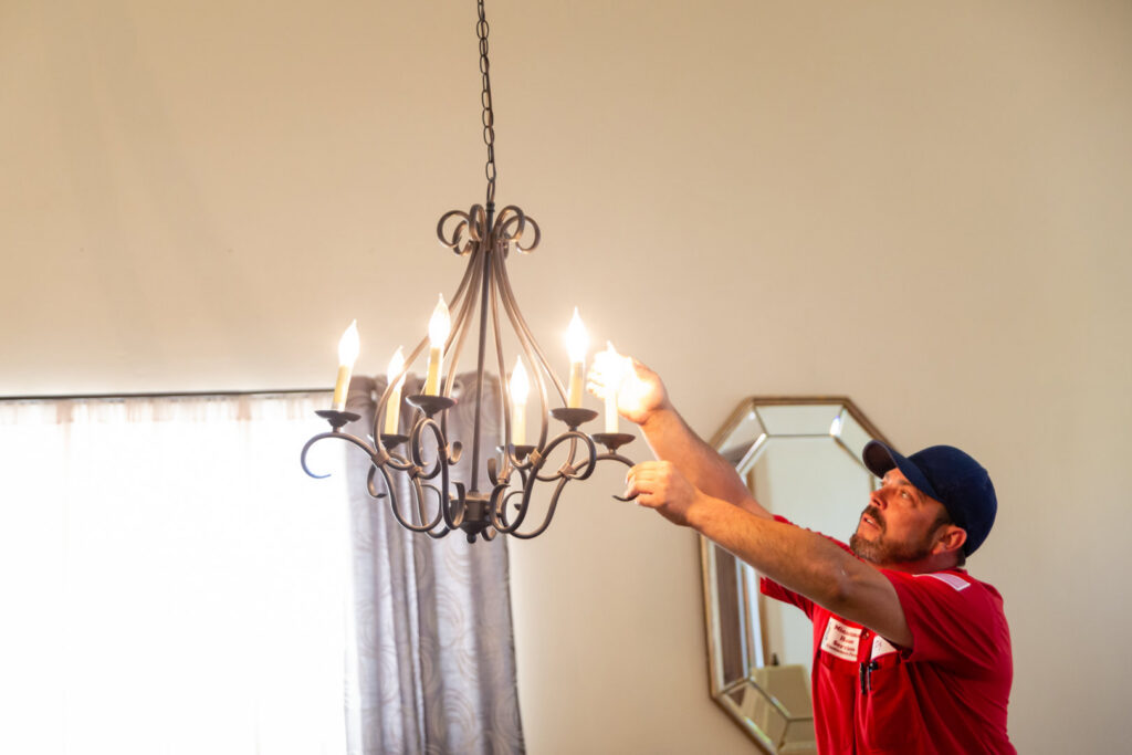 An electrician from Minuteman Home Services installing or repairing a chandelier in a home in Mesa, AZ