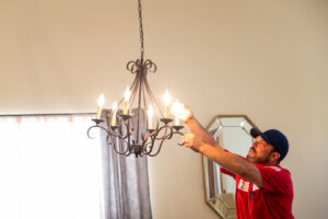 An electrician from Minuteman Home Services installing or repairing a chandelier in a home in Mesa, AZ